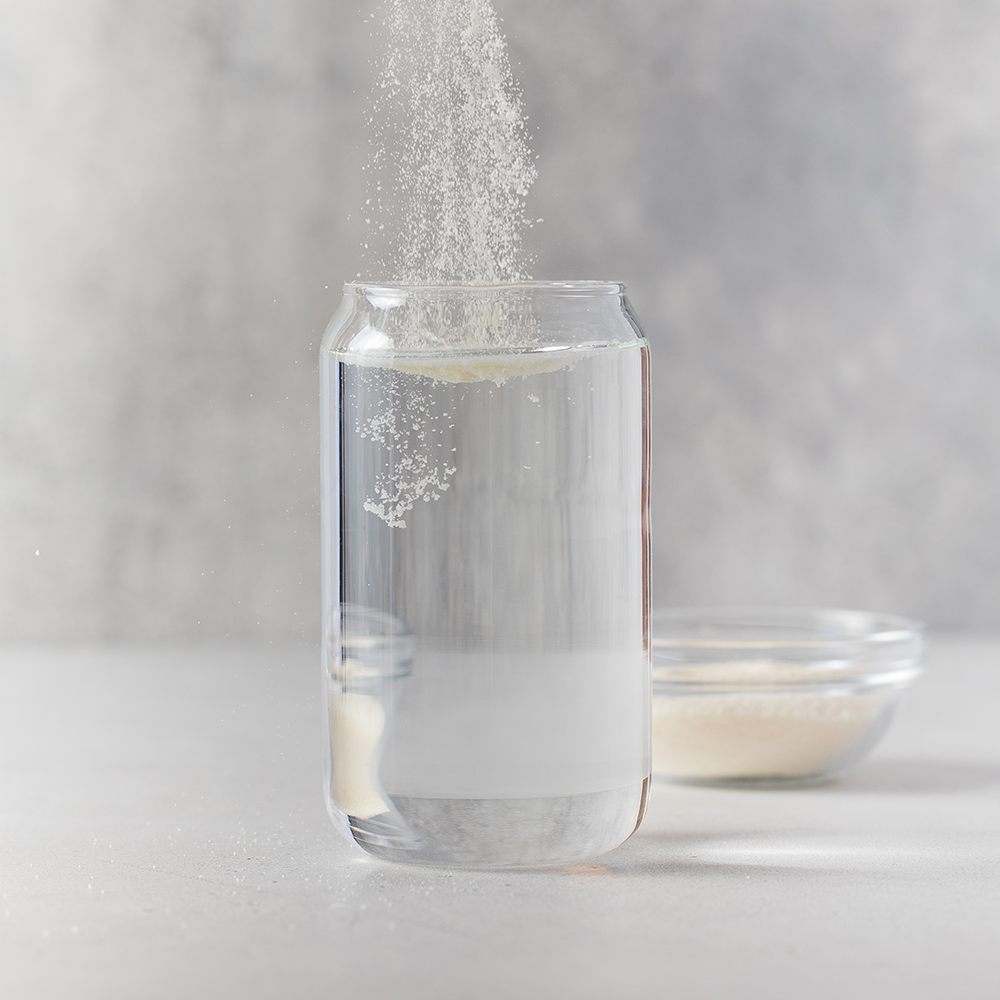 Poudre de collagène versée dans un grand verre d'eau