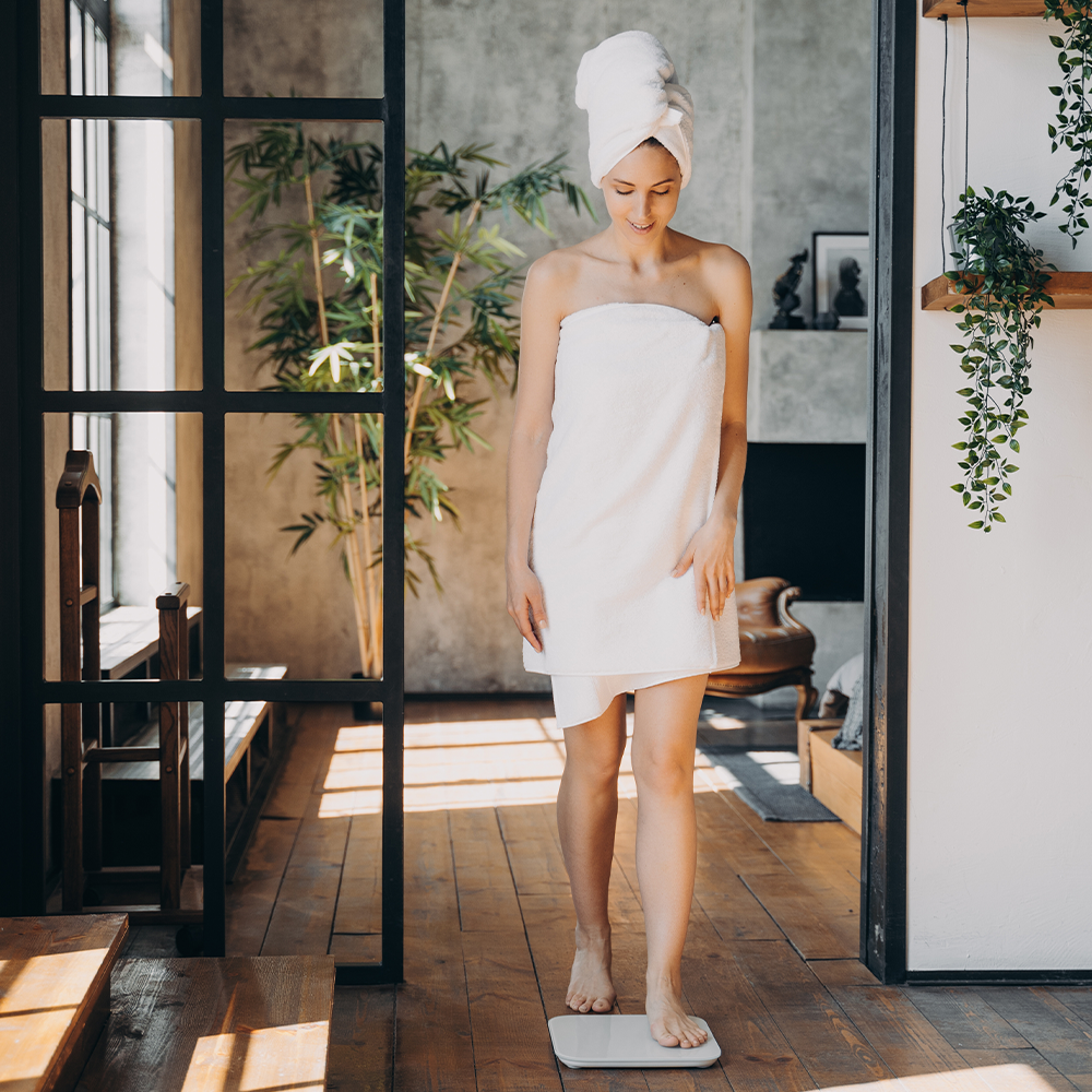 Une femme en peignoir monte sur une balance dans une salle de bain après sa douche