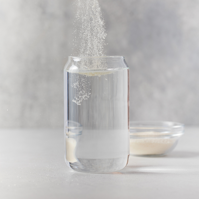 Poudre de collagène versée dans un grand verre d'eau