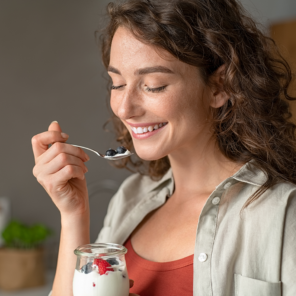 Femme souriante qui mange un yaourt avec des fruits