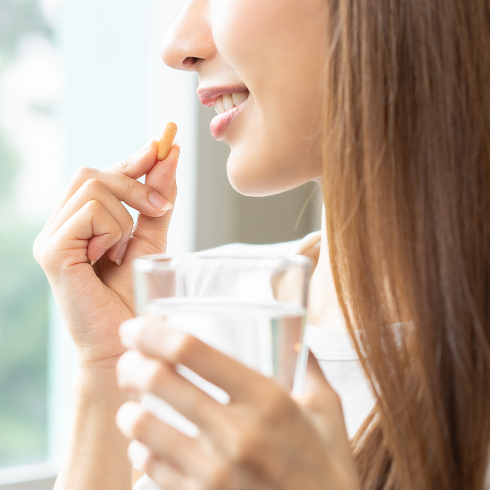 Jeune fille qui prend une gélule avec un verre d'eau dans une main