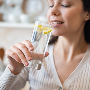 Jeune femme qui s'apprête à boire un grand verre d'eau avec du citron dedans