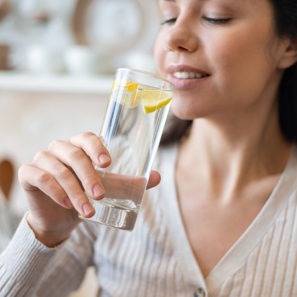 Jeune femme qui s'apprête à boire un grand verre d'eau avec du citron dedans
